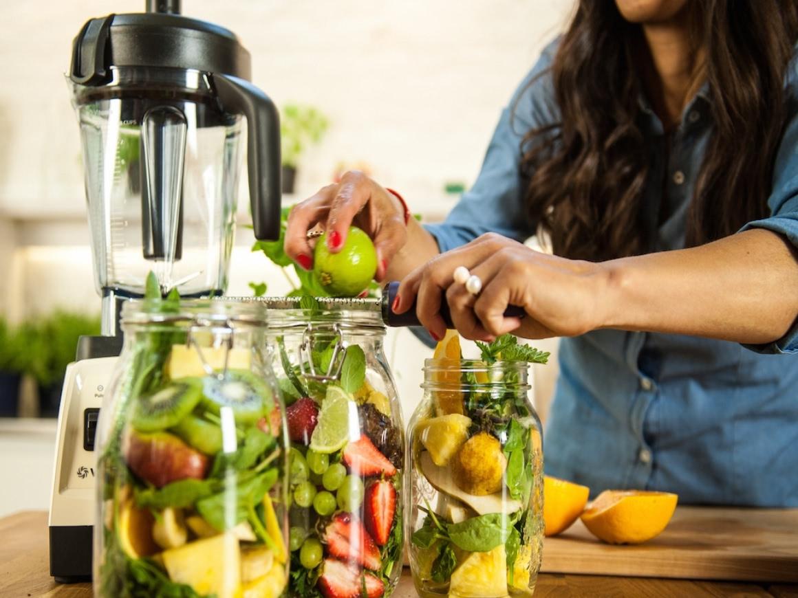 Three large jars filled with fruits and leafy greens for green smoothies.