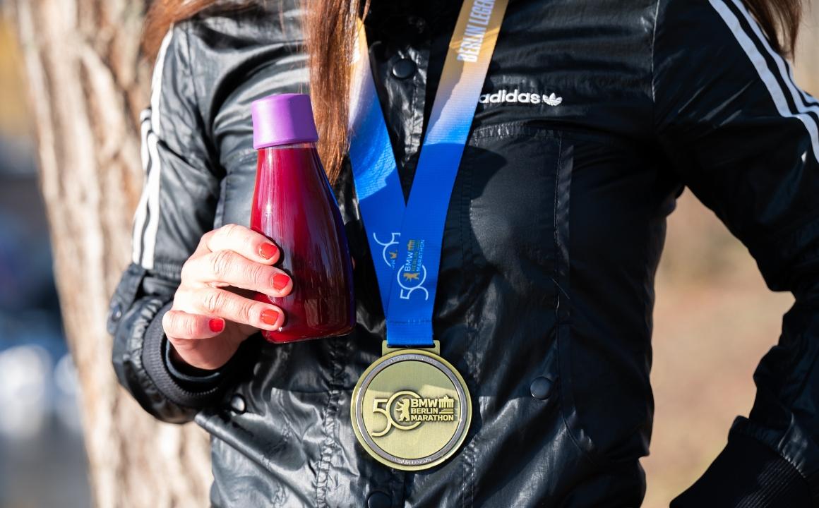 Runner with marathon medal and beetroot juice after a successful race