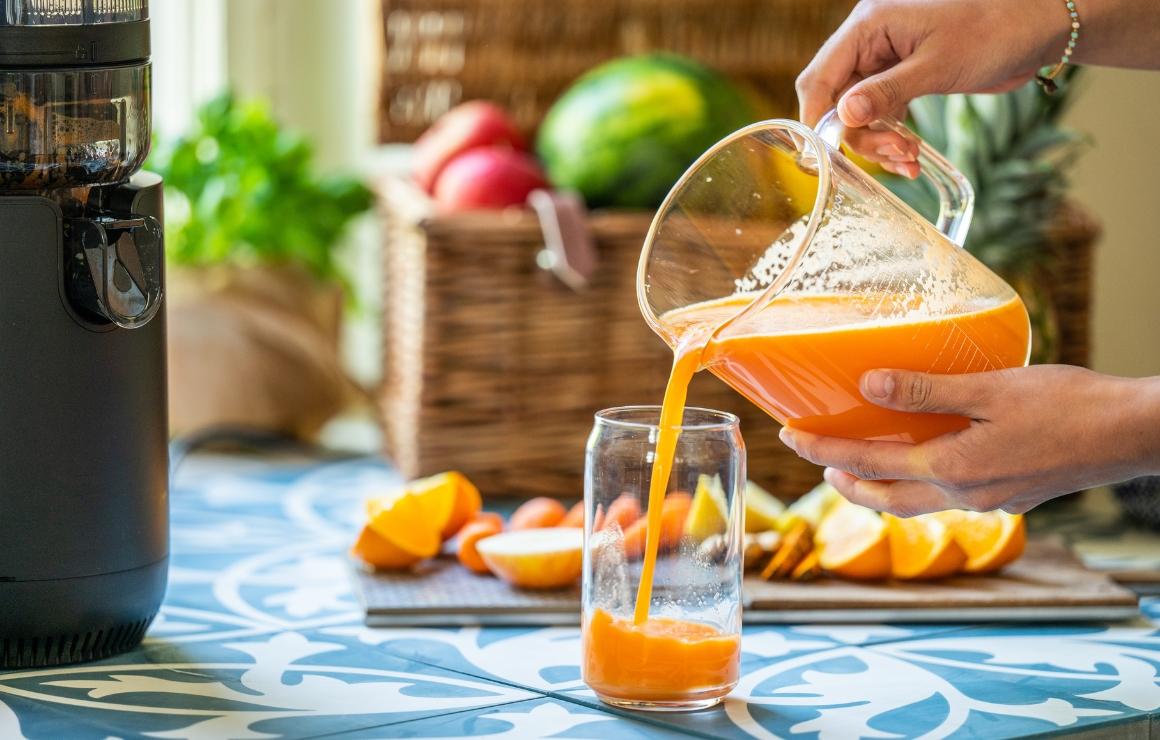 Viasus Flow M on the left, on the right clear, freshly pressed carrot juice being poured into a glass